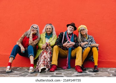 Group of carefree senior citizens looking at the camera while sitting together against a red background. Four vibrant elderly friends relaxing together in colourful clothing. - Powered by Shutterstock