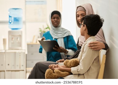 Group of caring Muslim professionals and child with teddy bear sitting in modern medical office, showing support and comfort during healthcare visit, affectionate interaction, diverse group - Powered by Shutterstock