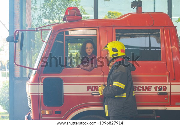 A group of caucasian firefighters or fireman team\
with uniform, a woman talking, working on their career. An\
emergency accident rescue. People. Hero teamwork with a fire truck\
car. Service job