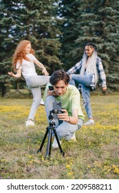 Group Of Caucasian Friends Filming Video Blog For Social Network, Using Cell Phone On Tripod To Broadcast In Summer Park. Video For Social Media Talking