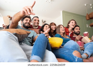 A group of Caucasian friends sitting on the couch and watching TV while eating popcorn, chips, and Chinese food. They enjoy each other's company and having fun together. - Powered by Shutterstock