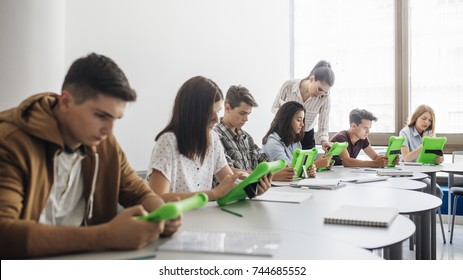 Group of Caucasian high school students studying together on tablets at round classroom.