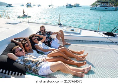 Group of Caucasian man and woman friends enjoy sunbathing and talking together while catamaran boat sailing at summer sunset. Male and female relax outdoor lifestyle on sail yacht travel vacation