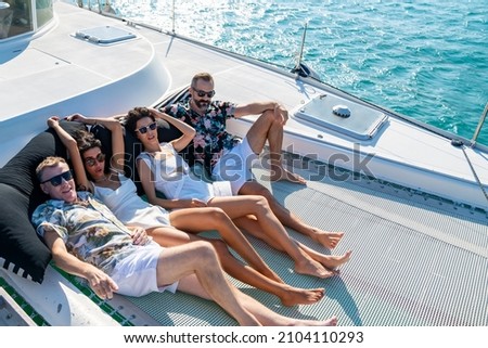 Group of Caucasian people resting together while catamaran boat sailing in the sea at summer sunset. Man and woman friends enjoy luxury outdoor lifestyle sail yacht on holiday travel vacation trip.