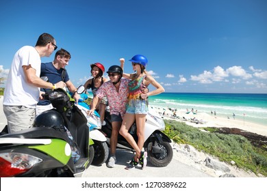 Group Of Caucasian People Standing Near Scooters Near Beach In Caribbean Sea And Talking With Each Other