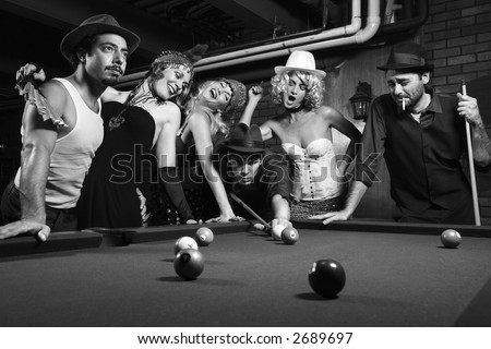 Group of Caucasian prime adult retro males and females trying to distract man as he takes pool shot.