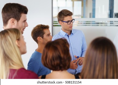 Group Of Caucasian Workers Standing Around Each Other In Small Office Glass Cubicle Setting