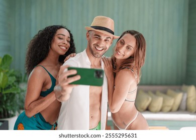 A group of cheerful diverse friends, clad in swimwear, capture a happy moment together with a selfie by a tranquil pool, radiating young adult vacation vibes. - Powered by Shutterstock