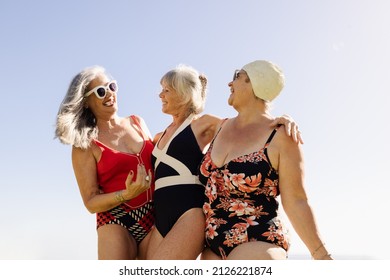 Group Of Cheerful Elderly Women Having Fun During Summer Vacation. Happy Senior Women Laughing And Embracing Each Other While Wearing Swimsuits. Mature Women Enjoying Themselves After Retirement.