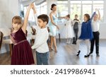 Group of cheerful emotional tweens, girls ad boys in formal wear dancing slow romantic partner dance in sunlit classroom during children festive event