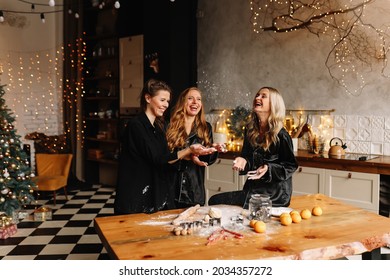 A group of cheerful female friends cook Christmas cookies, laugh, have fun and fool around in the kitchen in a cozy loft-style interior of the house, selective focus - Powered by Shutterstock