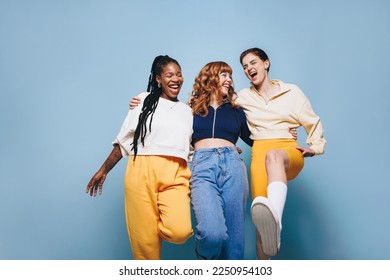 Group of cheerful female friends having fun while embracing each other. Three happy young women laughing and having a good time while standing against a studio background. - Powered by Shutterstock