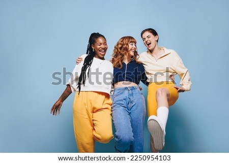 Group of cheerful female friends having fun while embracing each other. Three happy young women laughing and having a good time while standing against a studio background.