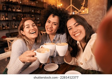 Group of cheerful female friends take a selfie toasting cups of cafe in coffee shop. Smiling and happy young girls looking at camera and having fun together. Women active on social networks. - Powered by Shutterstock