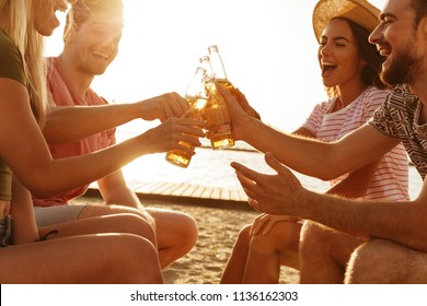 Group Of Cheerful Friends Dressed In Summer Clothing Toasting With Beer Bottles At The Beach