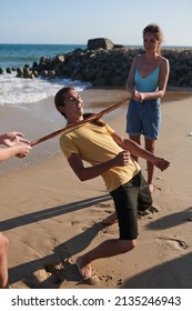 Group Of Cheerful Friends Ing Limbo Game On Beach, Summer Vacation Concept