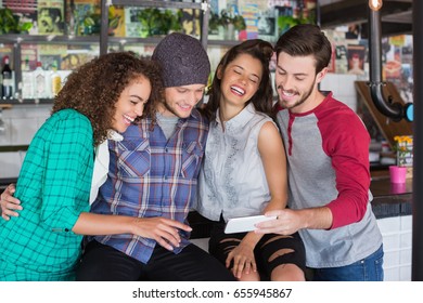 Group Of Cheerful Friends Laughing While Watching Mobile Phone In Restaurant