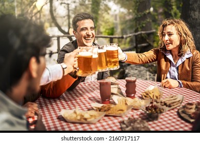 Group Of Cheerful Friends Toasting Beer Glasses - Happy People Partying And Eating In Farmhouse Garden - Young Active Adults In A Picnic Area With Snack And Drinks