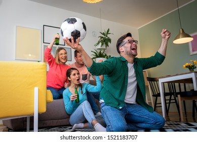 Group of cheerful friends watching soccer match and celebrating victory at home. Man on his knees cheering for his team.	