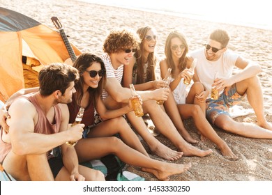 Group Of Cheerful Happy Friends Camping At The Beach, Drinking Beer