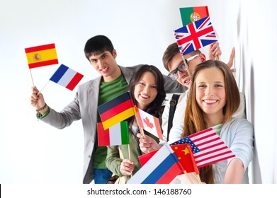 Group of cheerful happy students holding international flags and looking at camera leaning on white wall at campus. International education concept