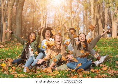 Group of cheerful international friends playing with autumn leaves in public park, taking autumn photos together - Powered by Shutterstock