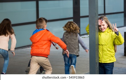 Group of cheerful kids playing hide-and-go-seek in street