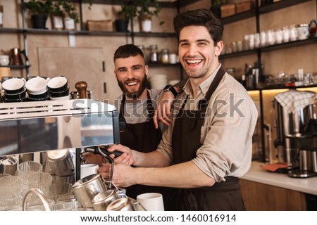 Group of cheerful men baristas wearing aprons working at the counter in cafe indoors, talking