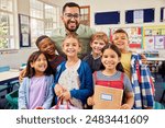 Group of cheerful multiethnic kids standing and posing for a photograph with male teacher at the end of the school year. Portrait of enthusiastic male teacher with his primary students in classroom.