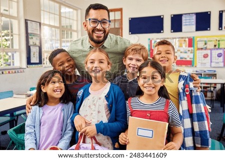 Group of cheerful multiethnic kids standing and posing for a photograph with male teacher at the end of the school year. Portrait of enthusiastic male teacher with his primary students in classroom.