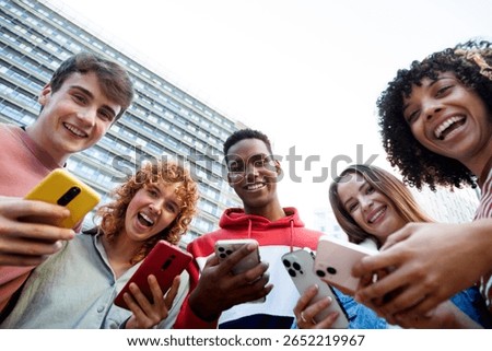 Group of cheerful multi-ethnic students using smartphones together in a university campus, enjoying mobile technology and social connection