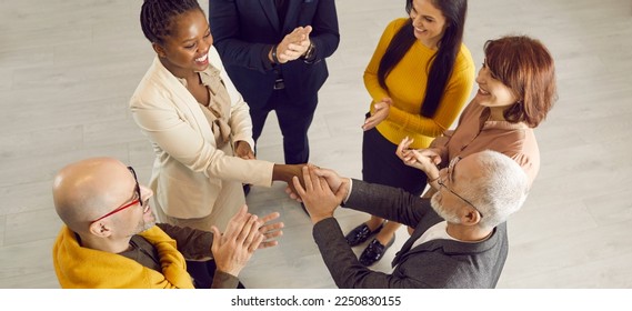 Group of cheerful positive diverse multiethnic people meeting and getting acquainted at casual business event. Young black woman feeling at ease and exchanging handshake with senior man. High angle - Powered by Shutterstock