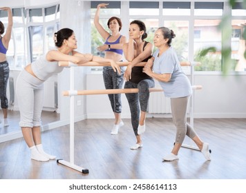 Group of cheerful relaxed women of different ages casually socializing and stretching beside ballet barre after dance practice in amateur choreographic studio - Powered by Shutterstock