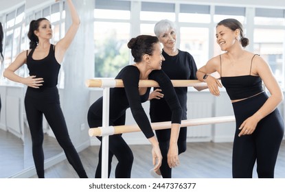 Group of cheerful relaxed women, young and mature, casually socializing and stretching beside ballet barre after dance practice in bright choreography studio - Powered by Shutterstock