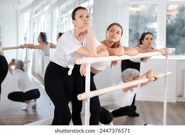 Group of cheerful relaxed women, young and mature, casually socializing and stretching beside ballet barre after dance practice in bright choreography studio - Powered by Shutterstock