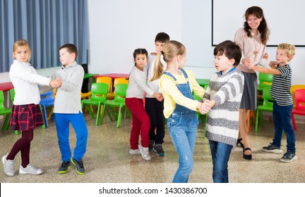 Group Of Cheerful School Kids Learning To Dance In Pairs With Their Teacher In Classroom On Recess