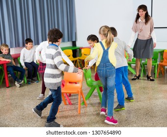 Group Of Cheerful School Kids Playing Active Games With Teacher In Classroom On Recess