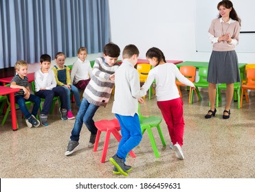 Group Of Cheerful School Kids Playing Active Games With Teacher In Classroom On Recess