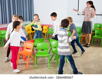 Group Of Cheerful School Kids Playing Active Games With Teacher In Classroom On Recess