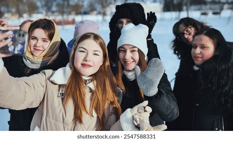 Group of cheerful schoolgirls taking selfie and waving at camera while enjoying winter day in snowy park - Powered by Shutterstock