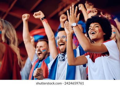 Group of cheerful sports fans celebrating victory of their favorite team while spectating game from stadium stands. Focus is on African American woman. - Powered by Shutterstock