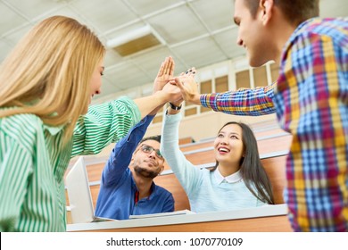 Group of cheerful students teaming up bumping fists in modern college auditorium, focus on  Middle-Eastern man and pretty Asian woman