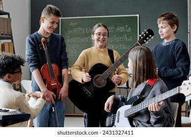 Group of cheerful teen boys and girls with musical instruments having break during rehearsal in classroom - Powered by Shutterstock