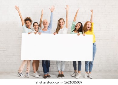 Group Of Cheerful Women Holding Blank White Poster Waving Hello Posing Near Brick Wall Indoor. Mockup