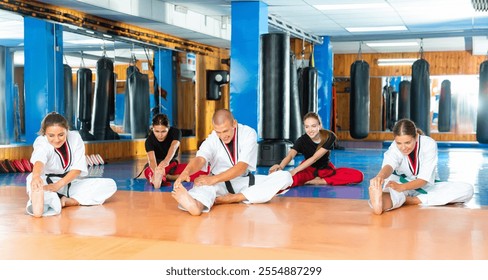 Group of cheerful women with man coach doing stretching before karate training at sport gym - Powered by Shutterstock