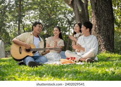 A group of cheerful young Asian friends are enjoying a picnic in a green park together, singing and playing guitar, eating yummy foods, and having a fun summer day together. Friendship concept - Powered by Shutterstock