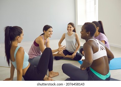 Group Of Cheerful Young Athletic Multiracial Women Communicating During Break In Yoga Studio. Women Share News And Exercise Tips And Making True Friends In Yoga Community. Group Sport Concept.