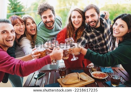 Group of cheerful young friends cheering with wine and beer glasses at picnic happy hour party in the terrace - Young people having fun drinking and eating outdoor - Friendship and youth lifestyle