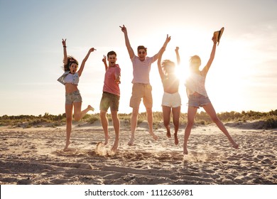 Grupo de jovenes amigos alegres vestidos con ropa de verano saltando juntos con las manos levantadas en la playa