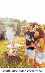 Group Of Cheerful Young Friends Having A Backyard Barbecue Party, Grilling Meat, Drinking Beer And Having Fun On A Sunny Summer Day